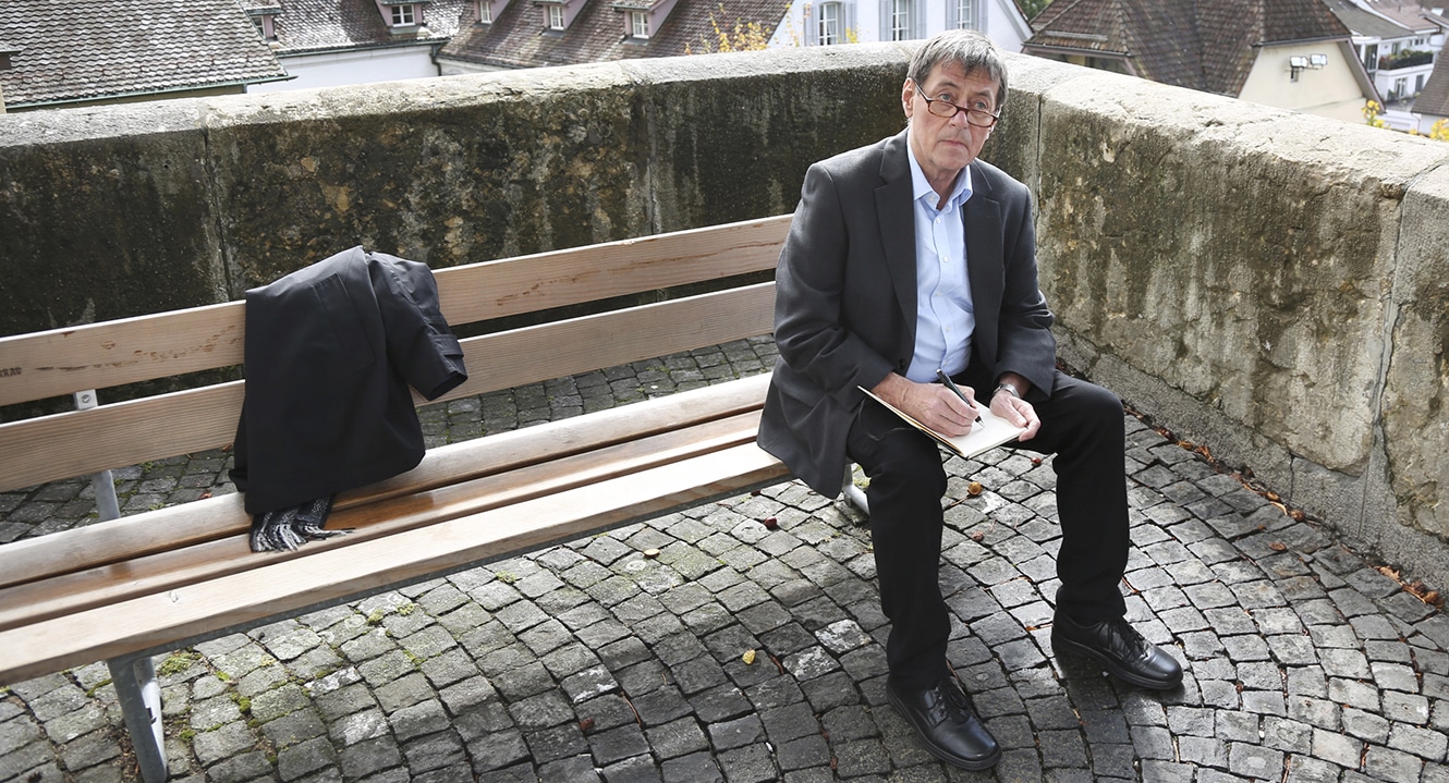 Trauerredner Jörg Bertsch sitzt auf einem Bänkli und notiert sich einige Gedanken.
